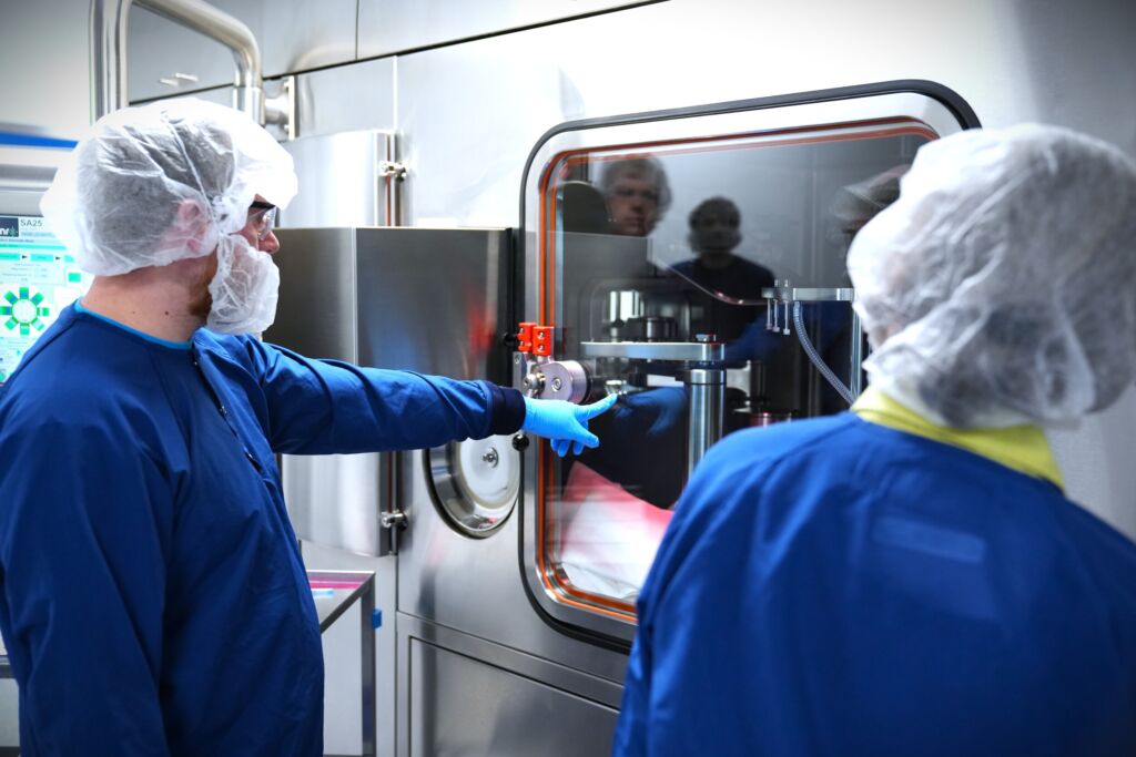 Two people in blue cleanroom gowns and hair nets operate a large stainless steel automated machine in a lab jun   updated market competitve jun   updated market competitve