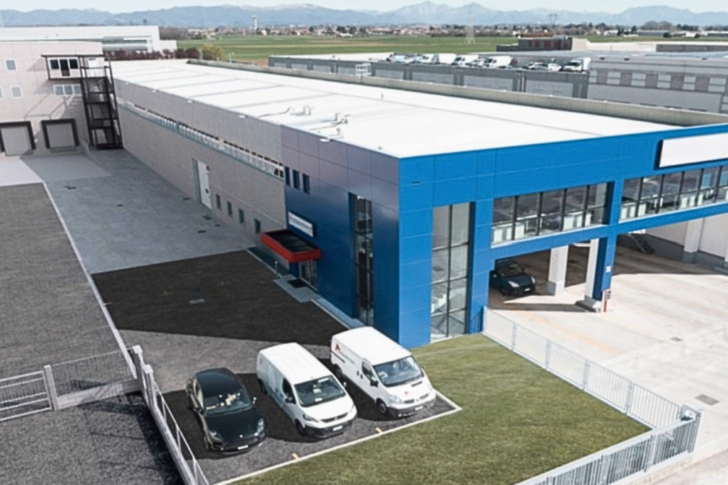 Aerial view of a modern commercial building with a bright blue façade glass entrances and a small parking area with white and black vans parked outside jun explore our facilities   rovello porro custom jun explore our facilities   rovello porro custom