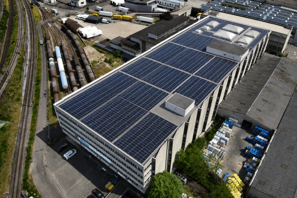 Aerial view of a large factory roof covered with solar panels beside a rail yard with freight cars and trucks nearby balerna switzerland custom balerna switzerland custom